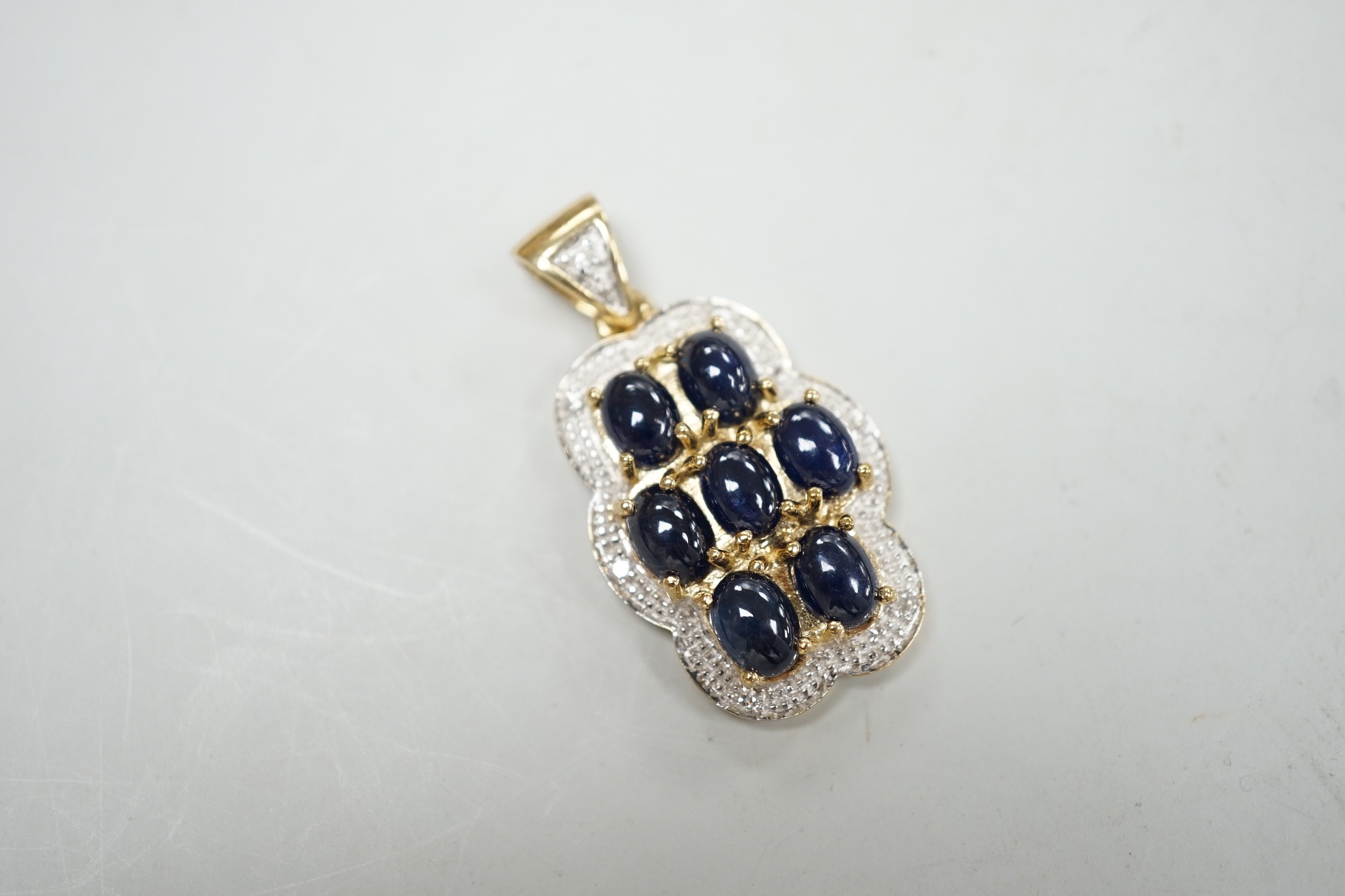 A modern 9ct gold, cabochon sapphire cluster and diamond chip set shaped oval pendant, overall 37mm, gross weight 8.4 grams.